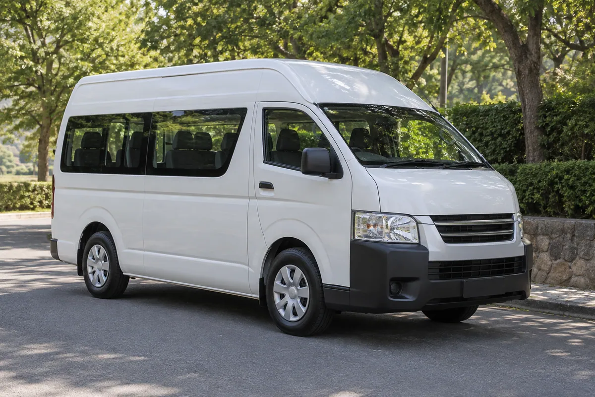 A white passenger minibus beside a tree-lined road